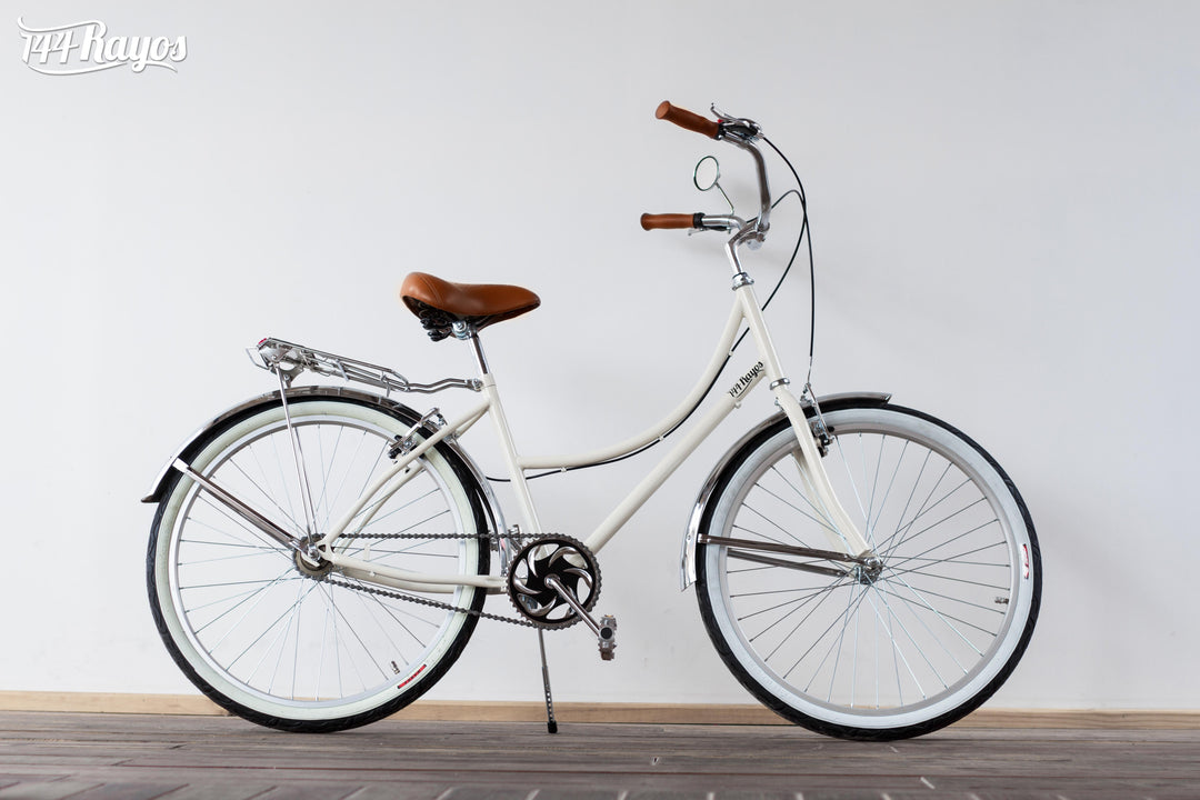 Bicicleta Cisne Blanco Cromado beige de cuadro bajo con llantas blancas, vista lateral sobre piso de madera