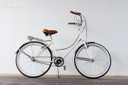 Bicicleta Cisne Blanco Cromado beige de cuadro bajo con llantas blancas, vista lateral sobre piso de madera
